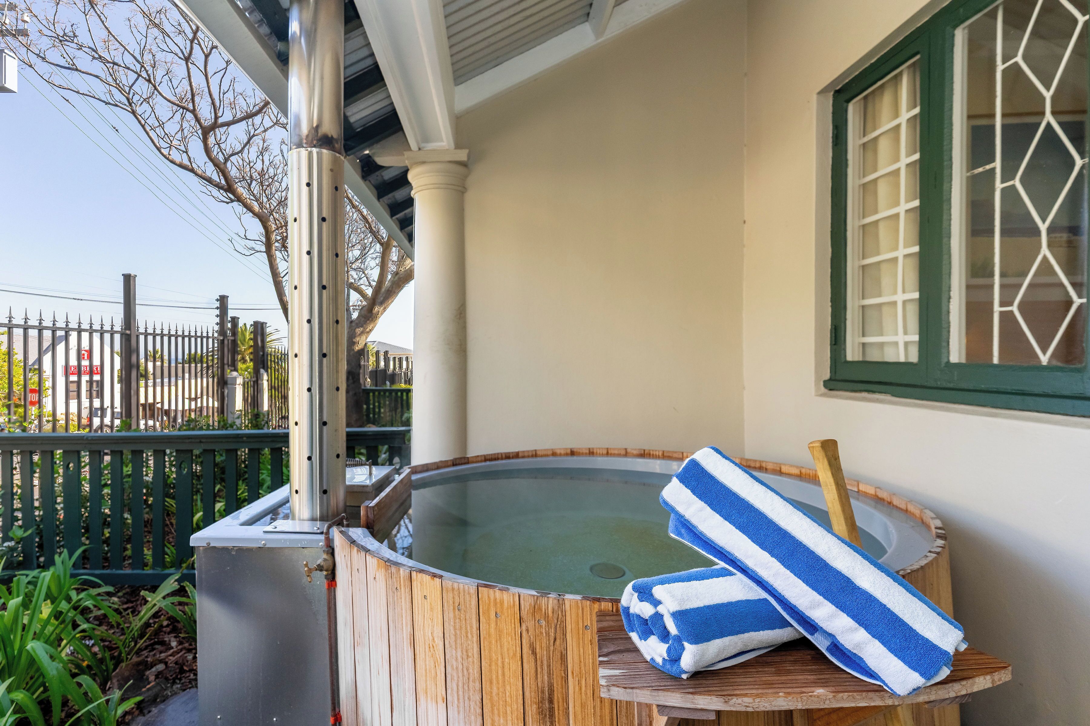 A wooden hot tub with a metal structure, a wooden table with a striped towel, and a window with a grid pattern.