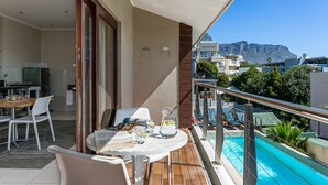 A balcony with a pool, a dining area with chairs and a table, and a kitchen visible through an open door.