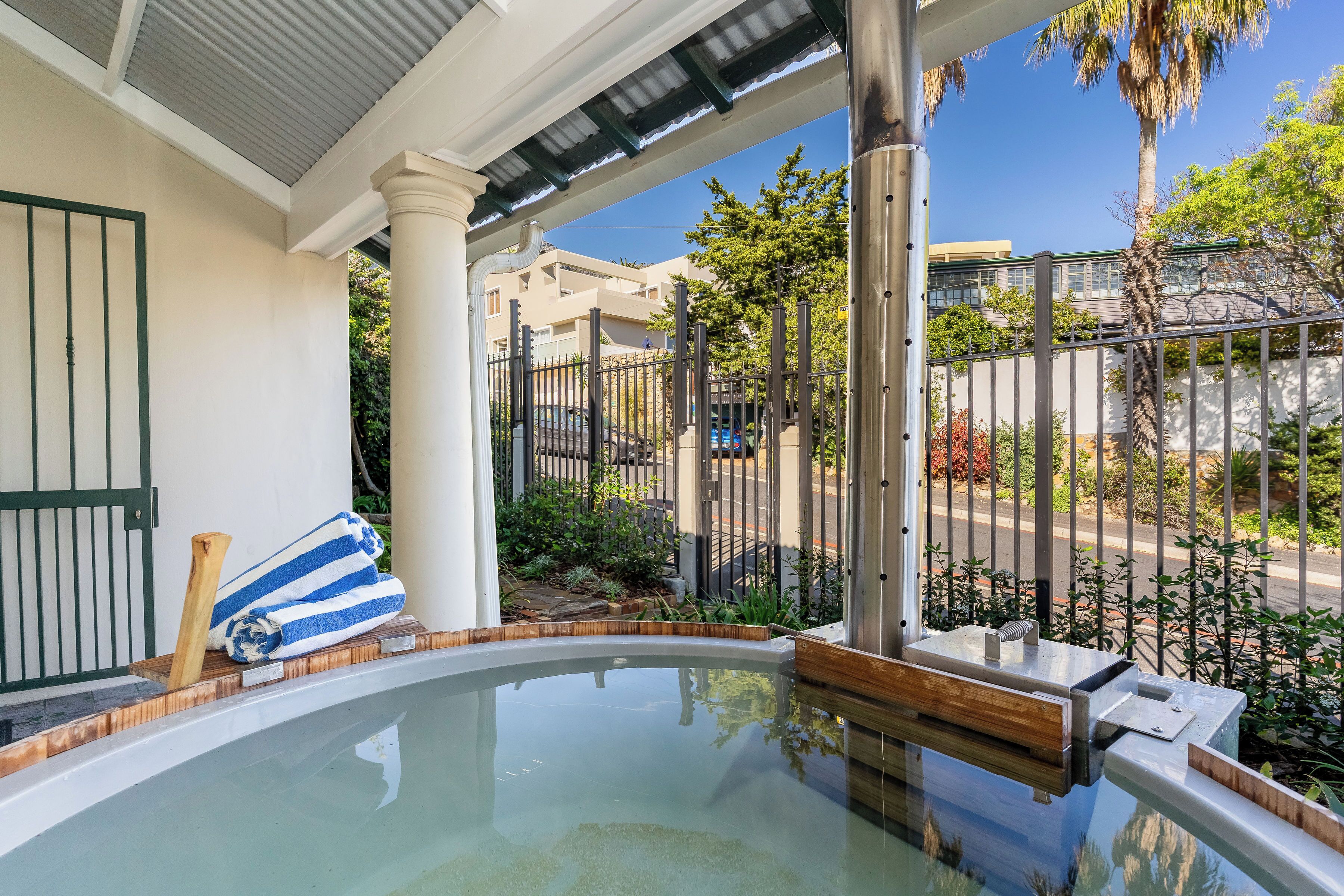 A pool area with a wooden bench and a blue towel, surrounded by a metal fence and palm trees.