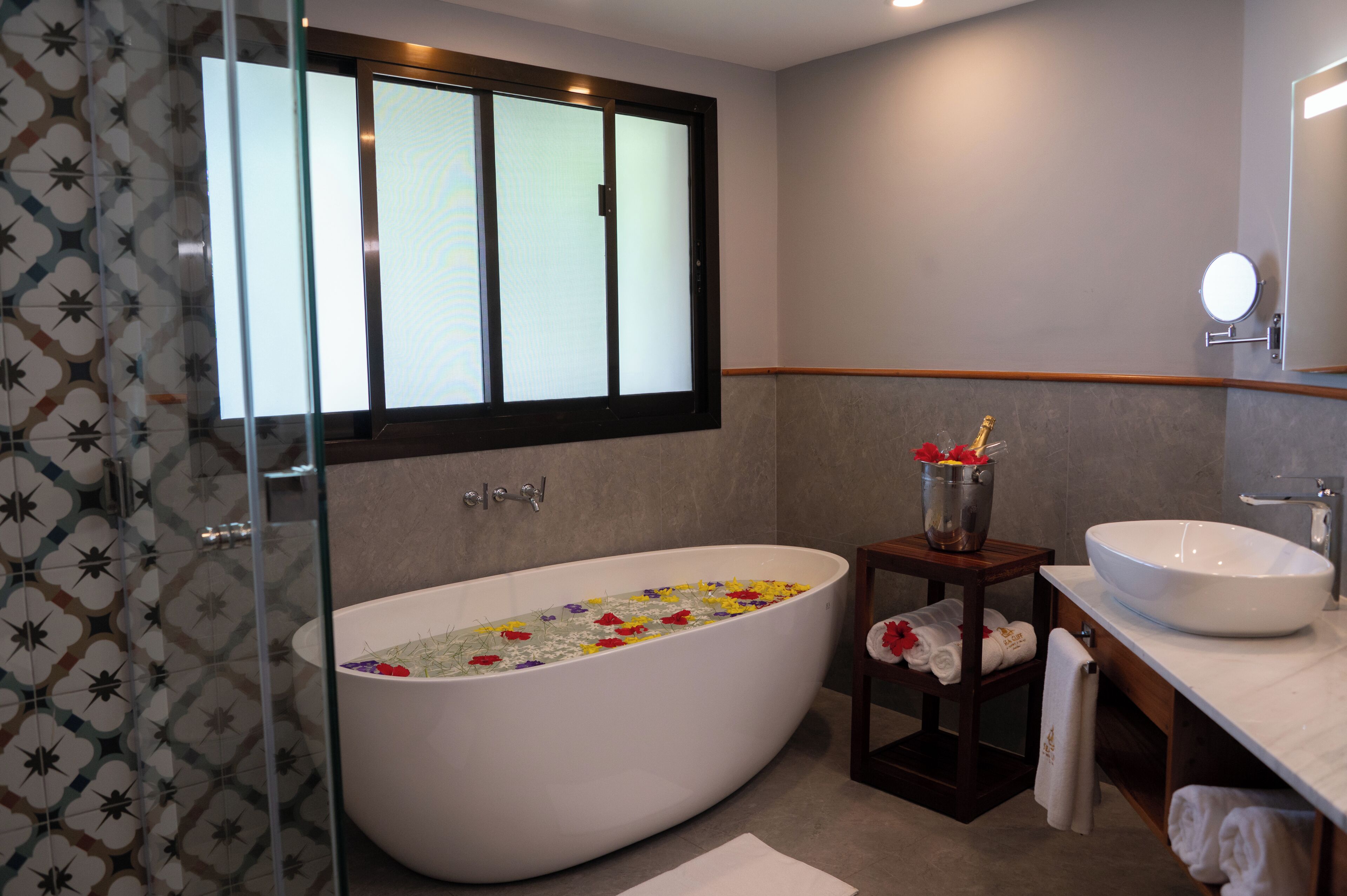 A modern bathroom with a freestanding bathtub, a large mirror, and a wooden shelf with towels.