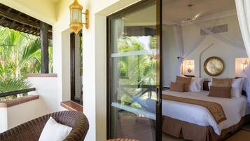 A hotel room with a balcony, a bed with white and brown bedding, a wicker chair, and a decorative wall lamp.