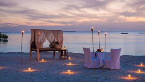 A beach setting with a canopy bed and a table set for two, surrounded by candles. - Sea Cliff Resort & Spa (Mangapwani)