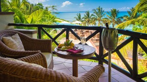 A wicker lounge chair and a small table with a tropical fruit plate, a glass of water, and a cocktail glass on a balcony overlooking a beach with palm trees and the ocean. - Sea Cliff Resort & Spa (Mangapwani)