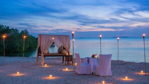 A beach setting with a canopy bed, a table with chairs, and candles. - Sea Cliff Resort & Spa (Mangapwani)