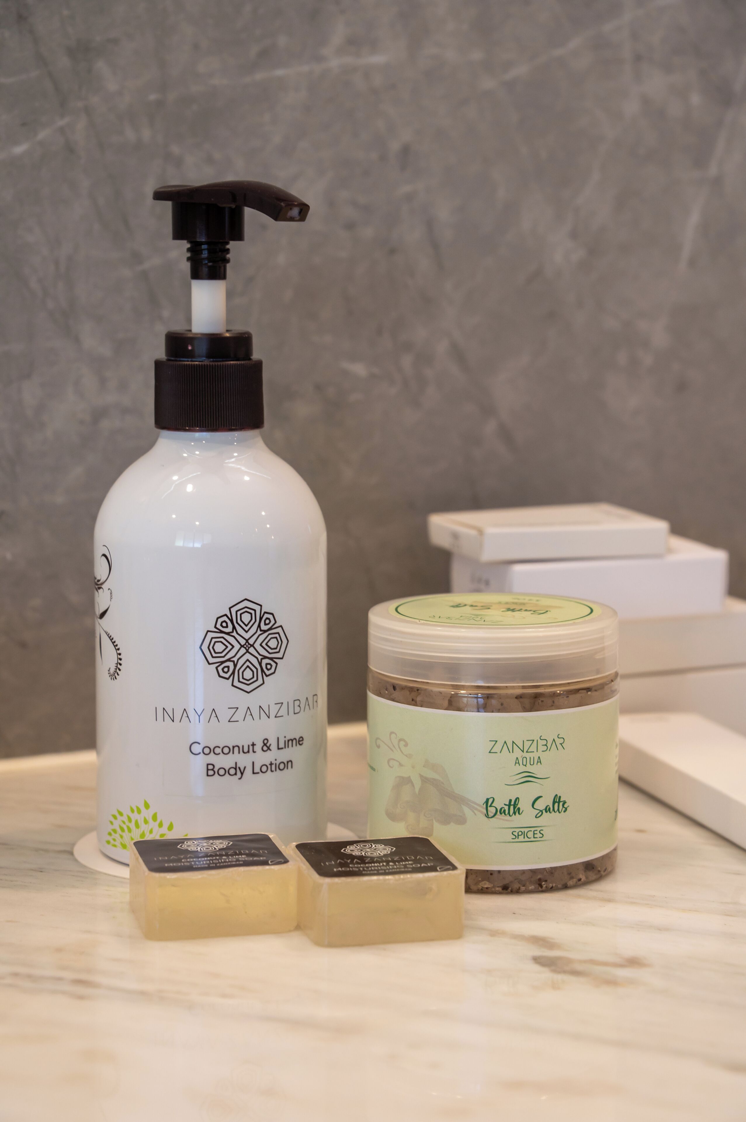 Un bagno con una bottiglia bianca di lozione corpo Inaya Zanzibar Coconut & Lime, un barattolo di sali da bagno e due saponette.