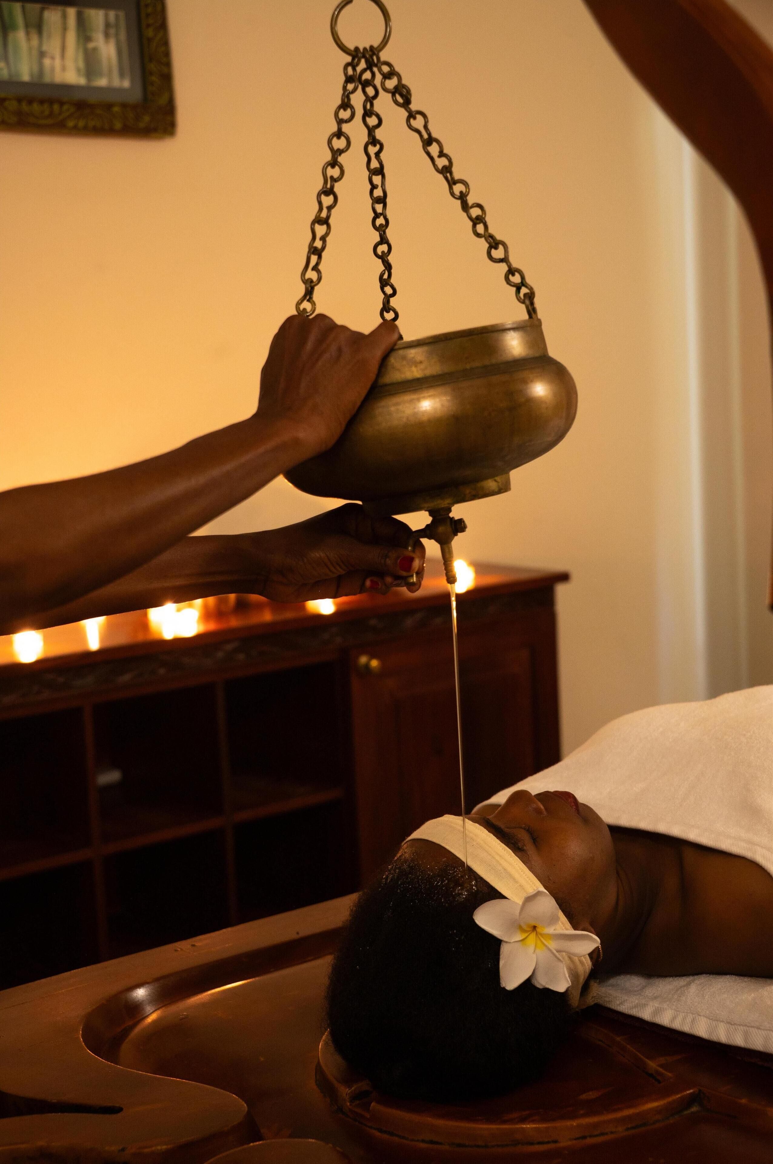 A person receiving a traditional treatment with a metal bowl and a lit candle.