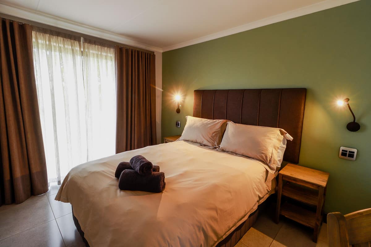 A neatly made bed with a headboard, a wooden nightstand, and a wall-mounted light fixture.