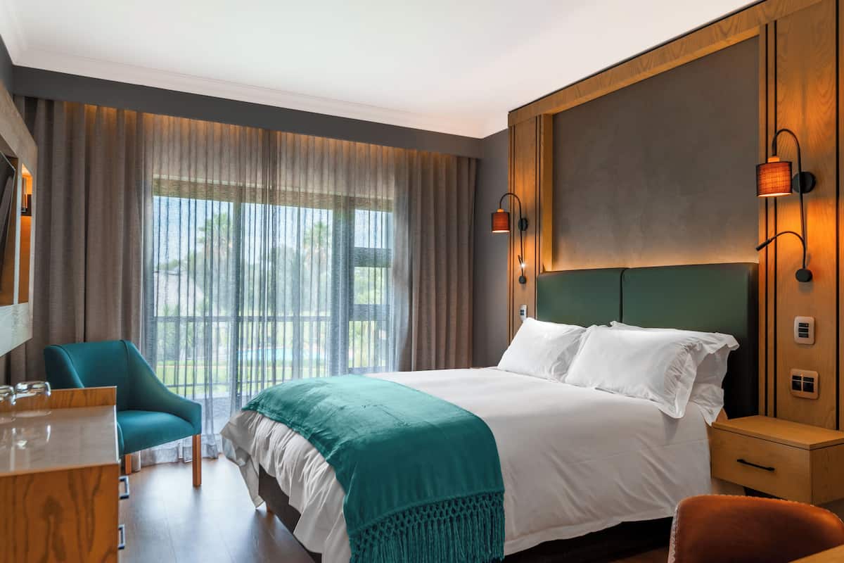 A hotel room with a large bed, a desk, a chair, and a view of the outdoors.