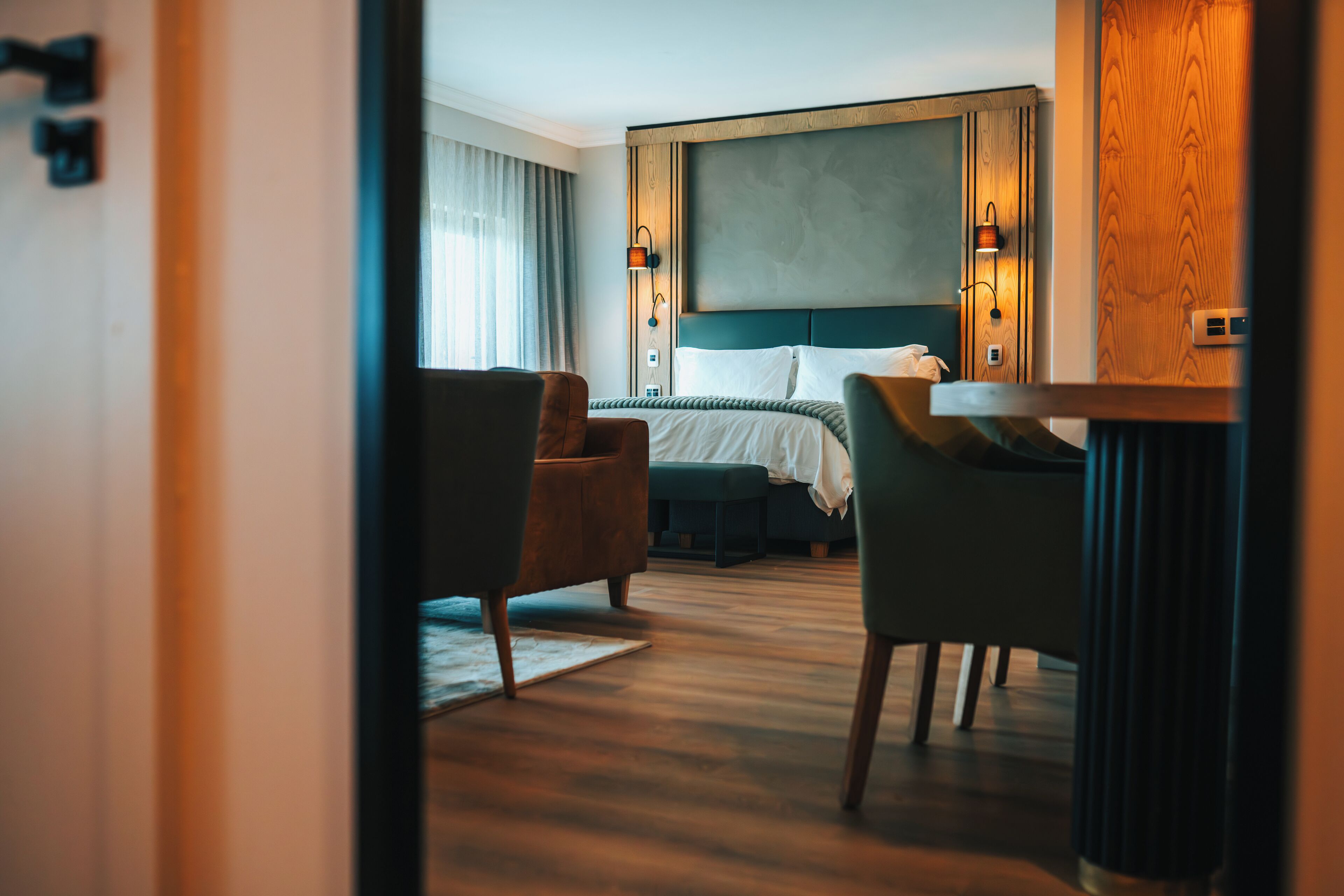 Une chambre d’hôtel avec un lit, deux chaises, une table et une grande fenêtre avec des rideaux.