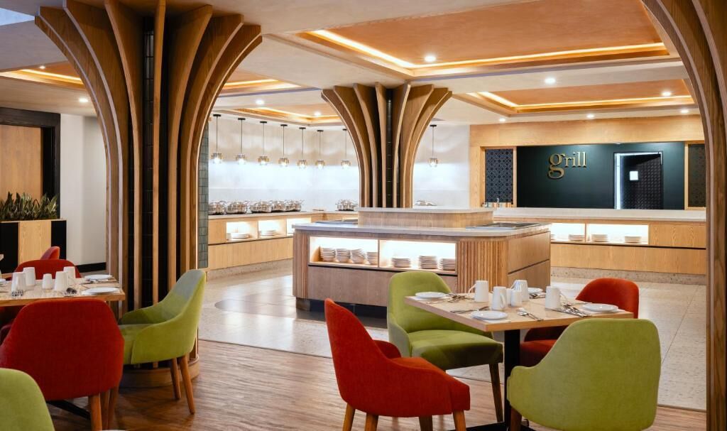 A modern restaurant with a central counter, vibrant chairs, and a 'Grill' sign on the wall.