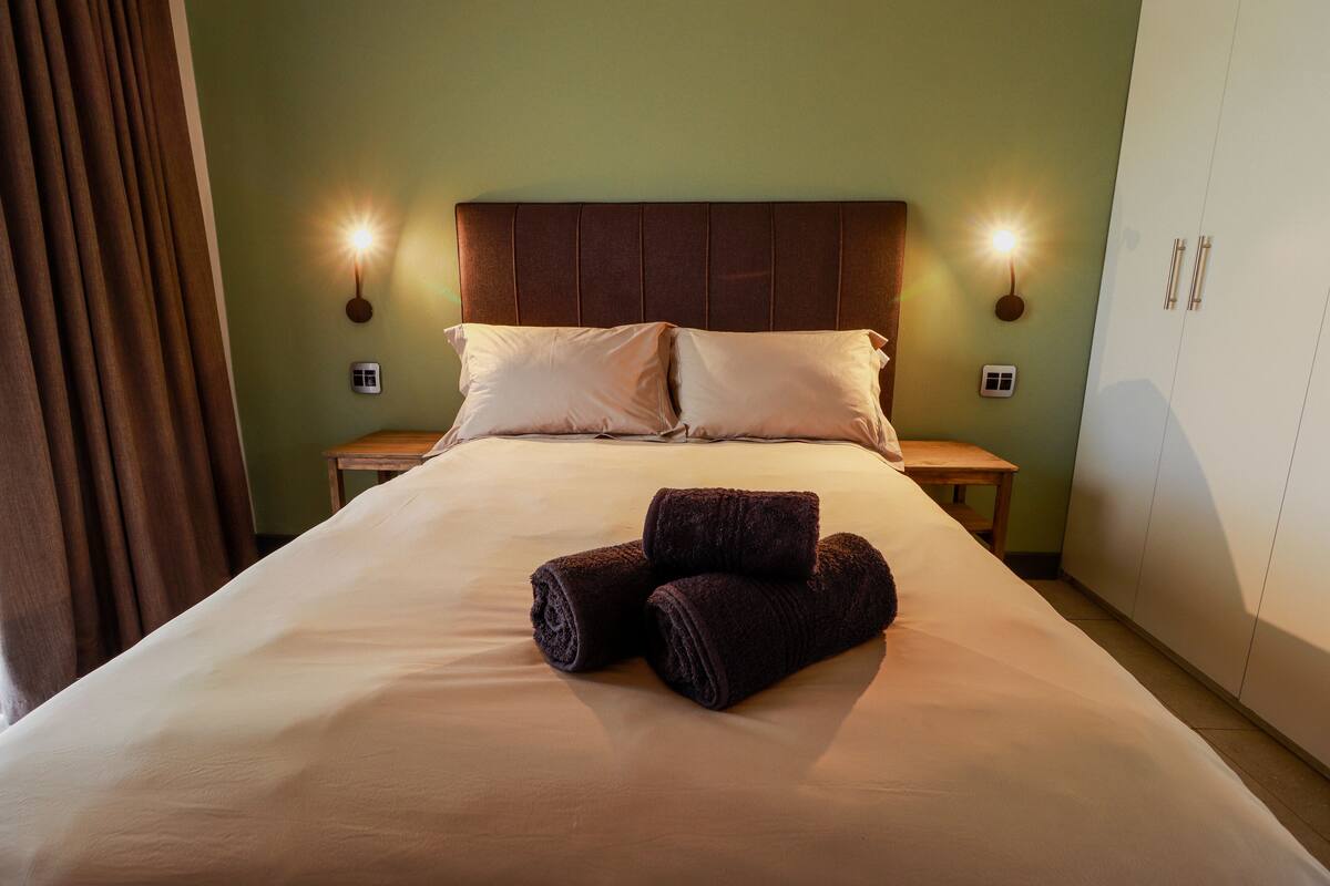 A neatly made bed with two pillows and two rolled towels in the center.