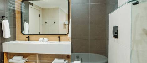 Une salle de bain moderne avec un grand miroir, un lavabo blanc et une douche séparée par des parois en verre.