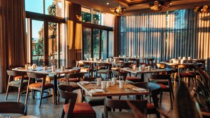 A restaurant with multiple tables and chairs, large windows, and a view of greenery outside. - Emerald Resort & Casino (Vanderbijlpark)