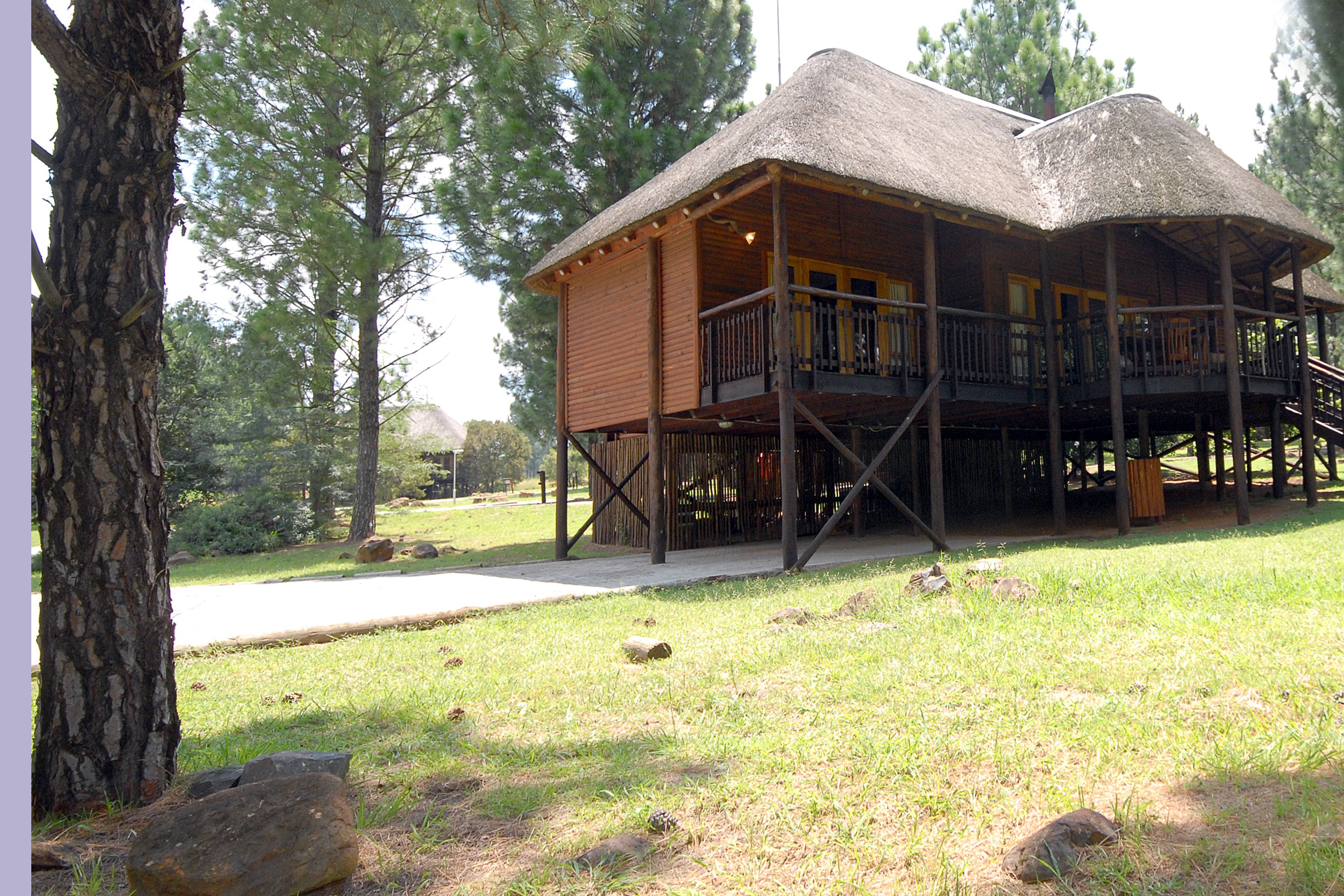 A wooden cabin with a thatched roof, a balcony, and a wooden deck.