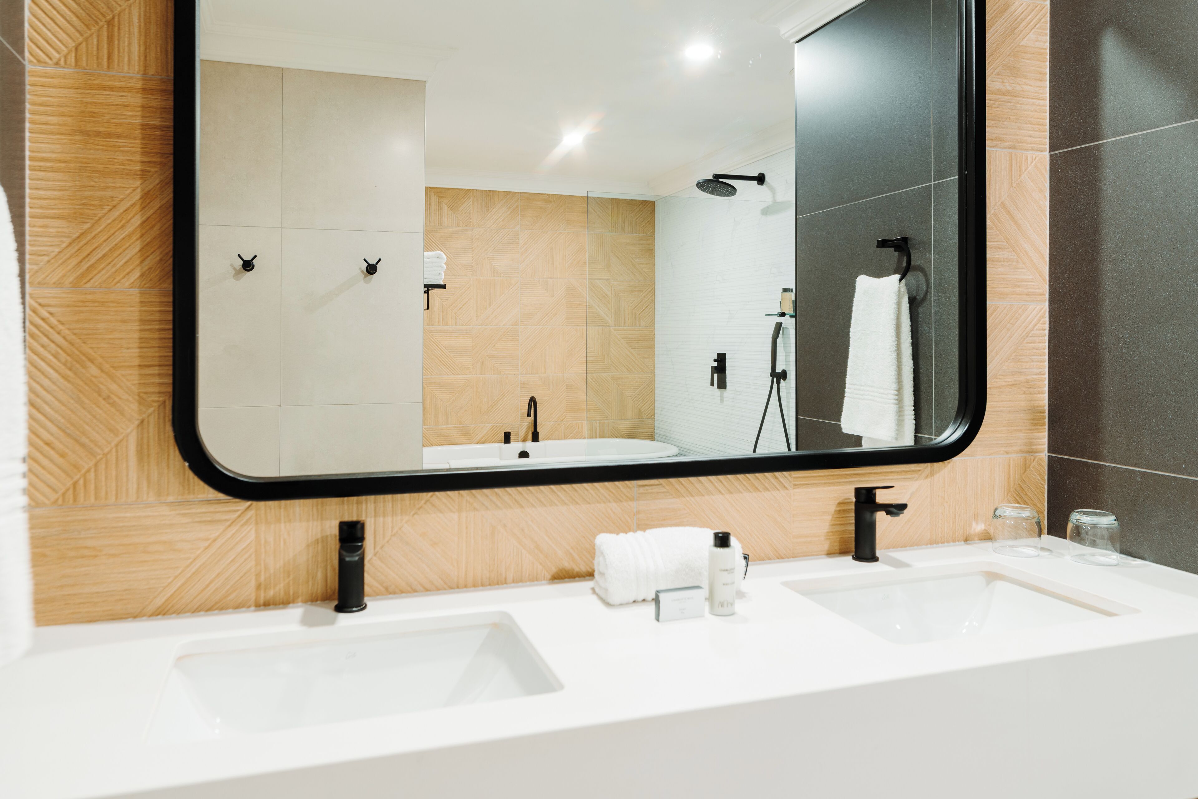 A modern bathroom with two sinks, a large mirror, and a shower.
