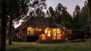 A rustic cabin with a thatched roof, a wooden deck, and a fire pit. - Emerald Resort & Casino (Vanderbijlpark)