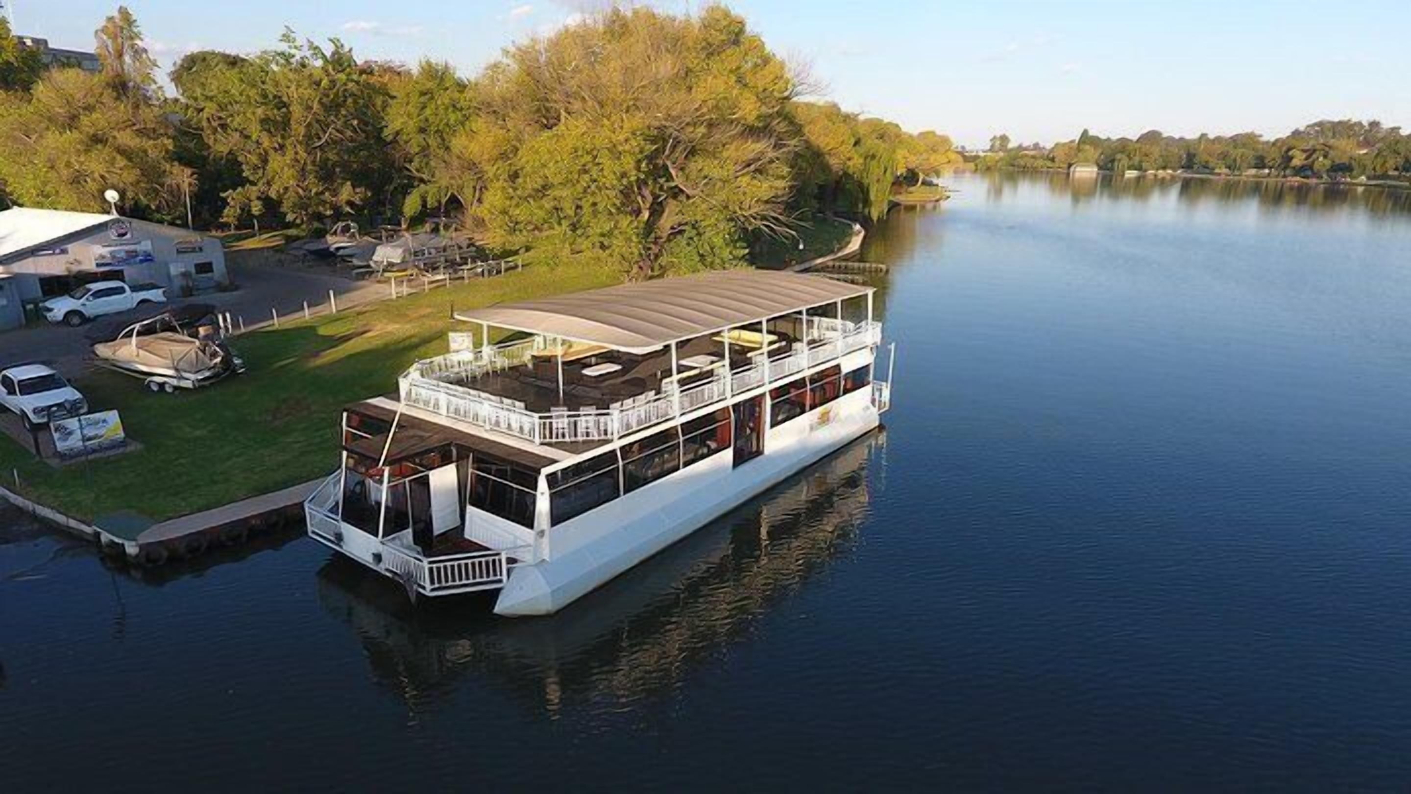 A large houseboat docked at a marina with a covered deck area and multiple levels.