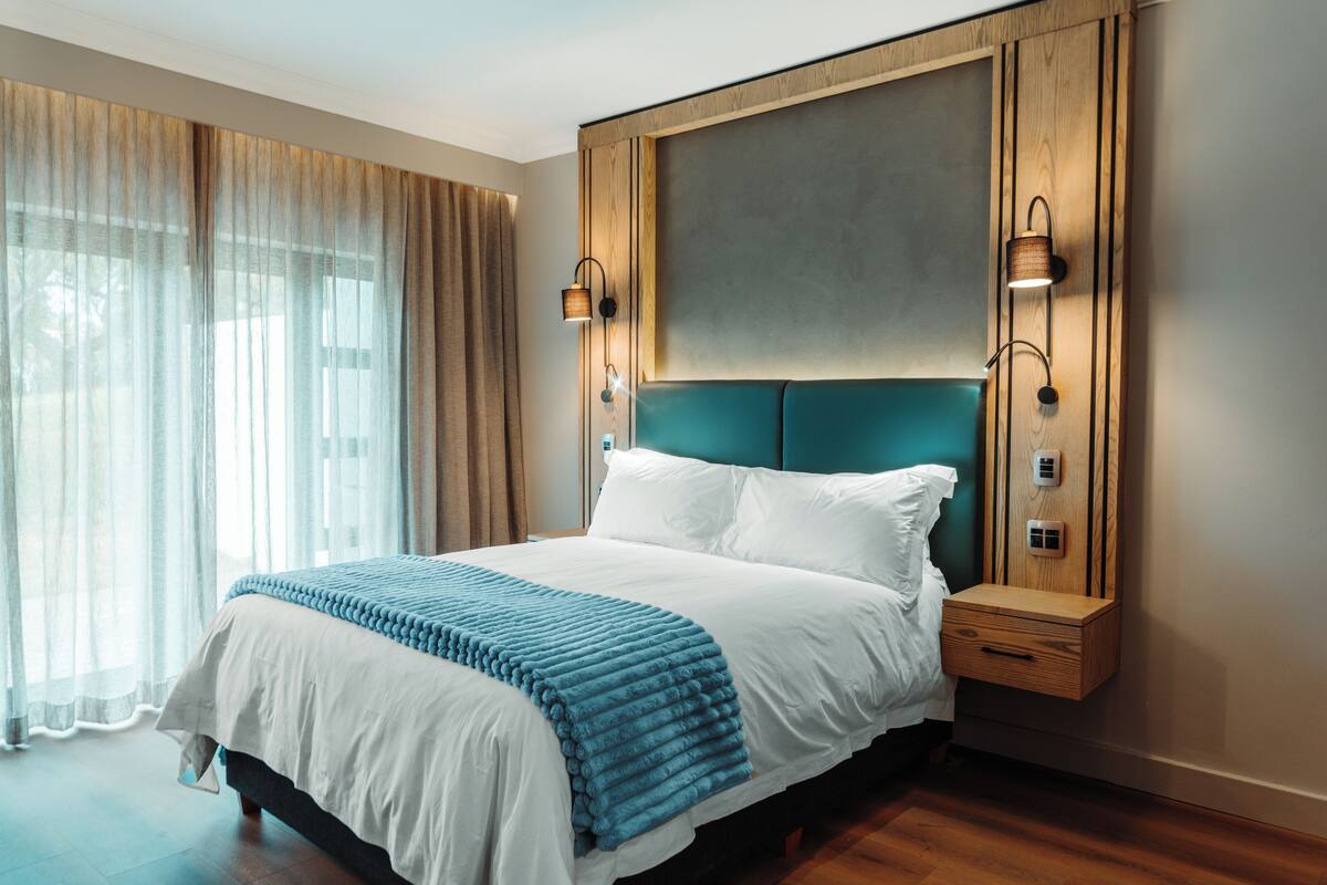 A modern hotel room with a large bed, wooden headboard, and two bedside lamps.