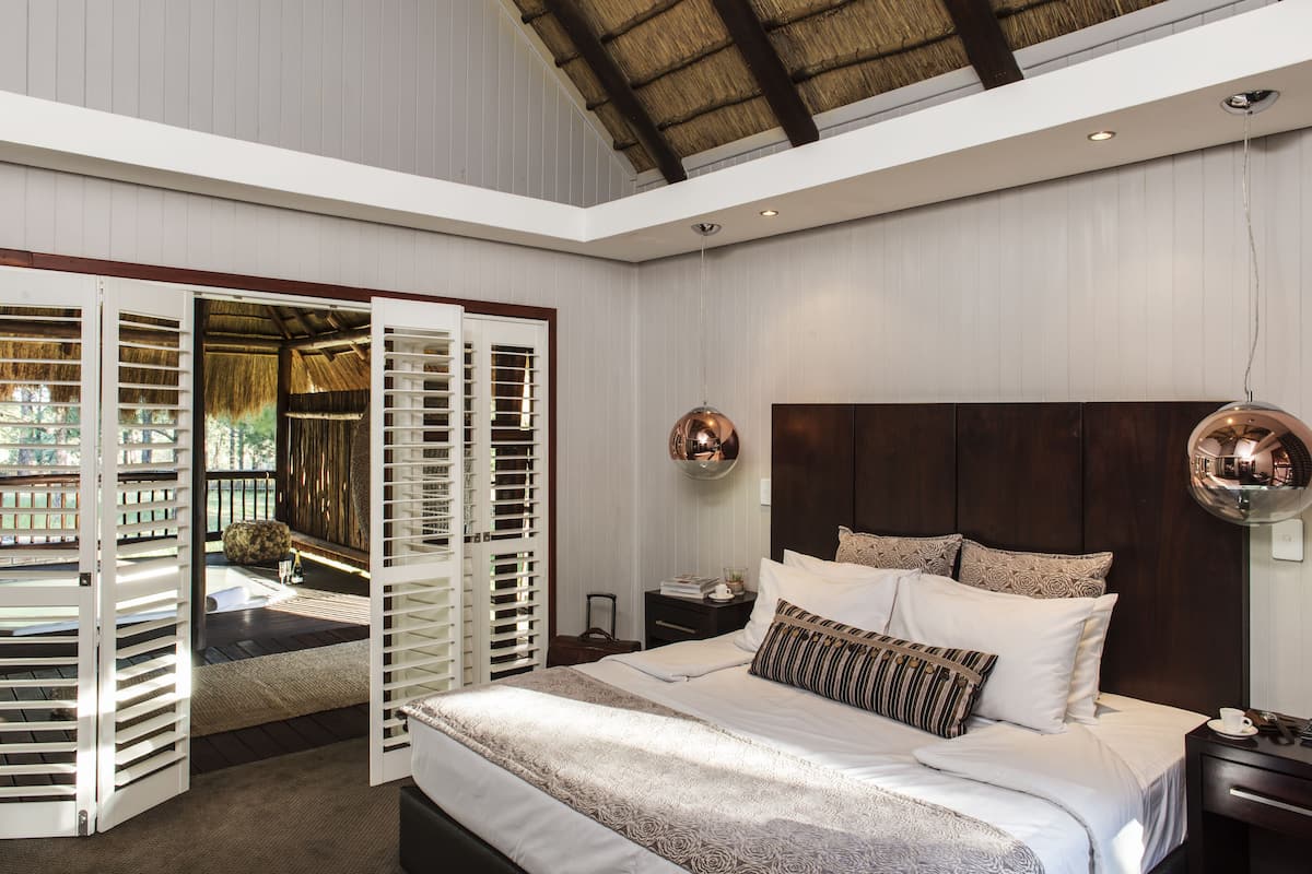 A bedroom with a large bed, a wooden headboard, a nightstand, and a hanging light fixture.