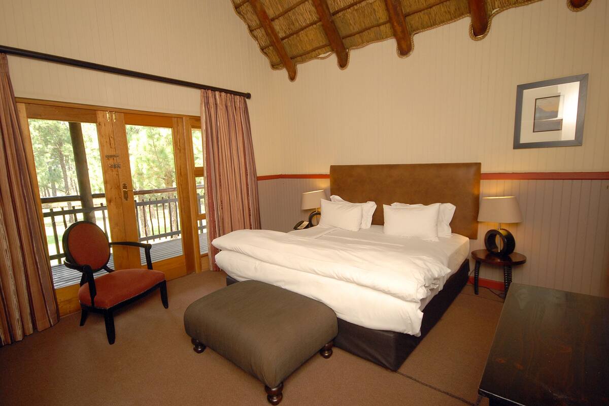 A hotel room with a large bed, a chair, an ottoman, a desk, and a view through a glass door.