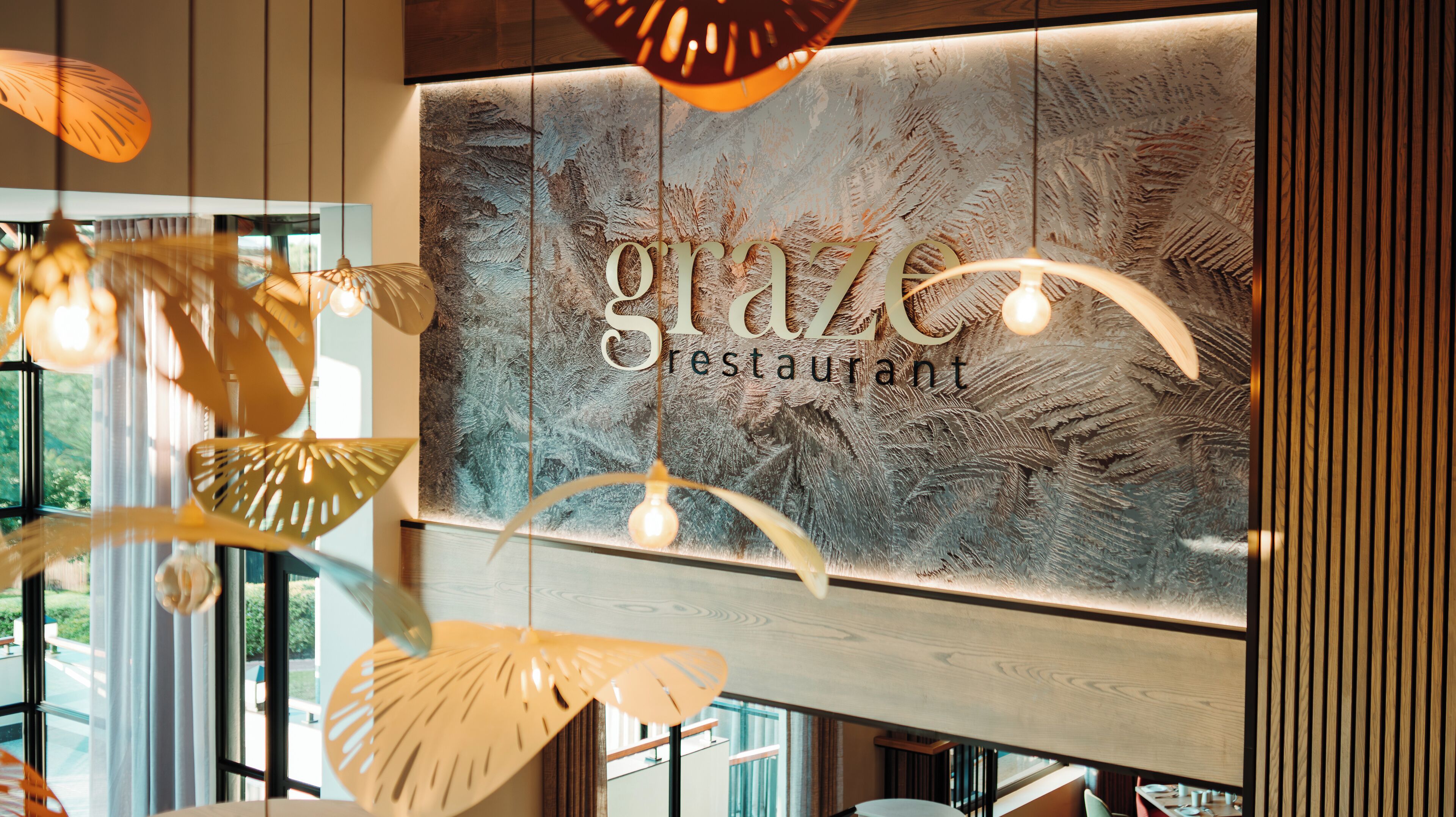 A restaurant interior with a modern design, featuring a large wall with the name 'glaze restaurant' and decorative hanging lights.