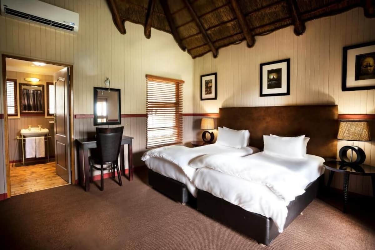 A hotel room with a large bed, a desk with a chair, a vanity with a mirror, and a window with blinds.