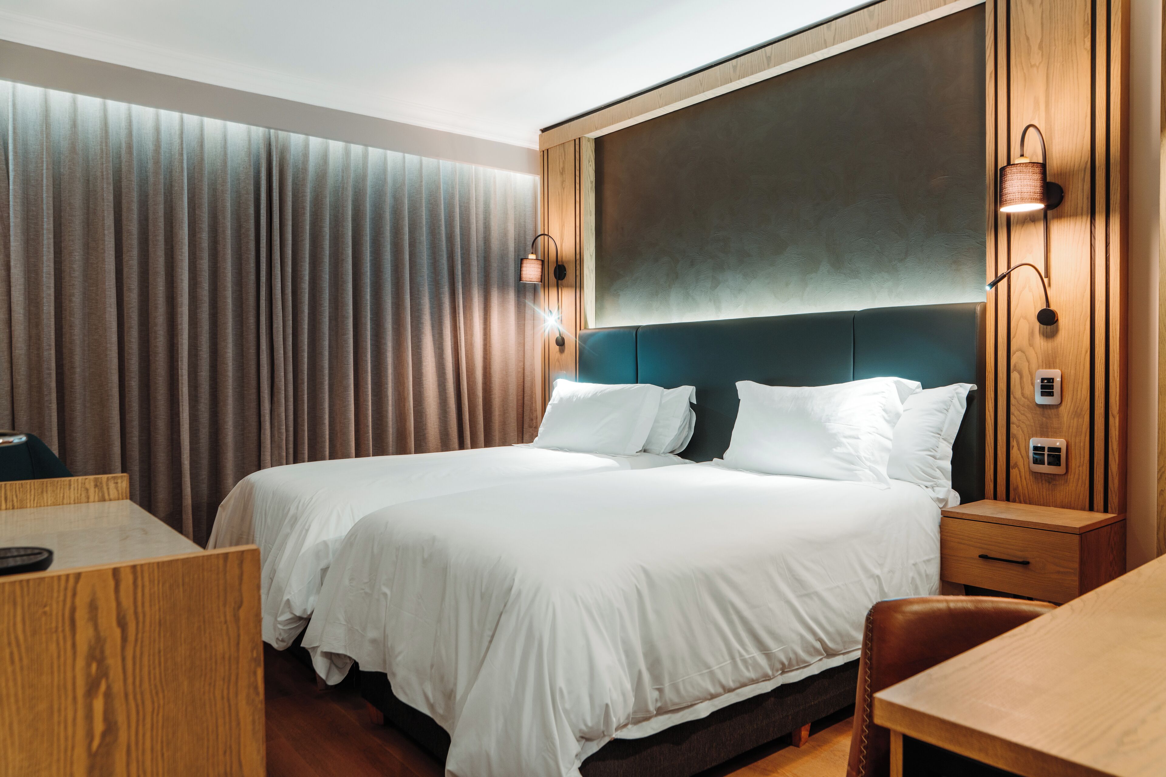 Una moderna camera d'albergo con un letto grande, una testiera in legno e illuminazione integrata.