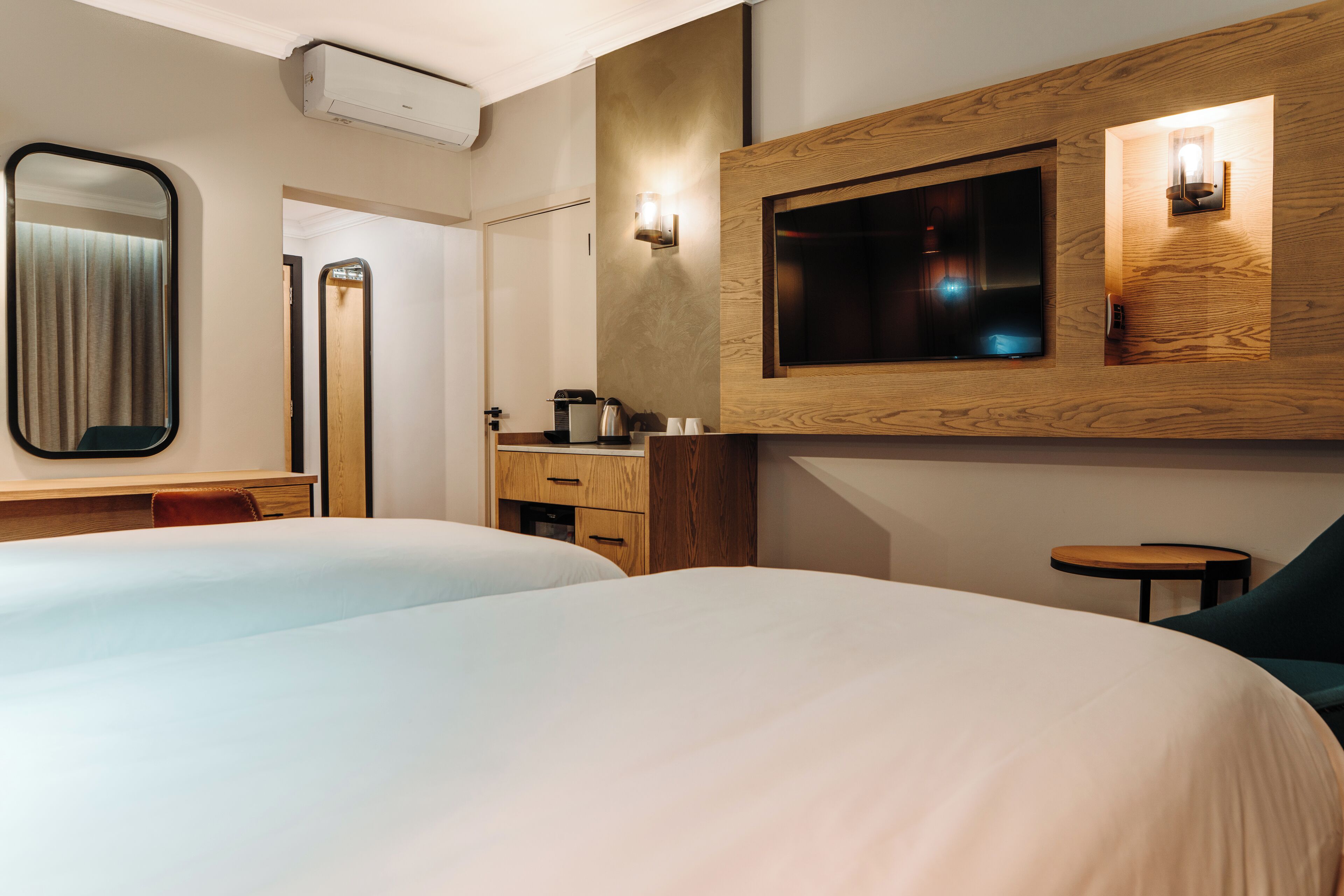 A hotel room with two beds, a wooden dresser, a mirror, a television, and a small table.