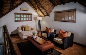 A cozy living room with a high ceiling, a sofa, two armchairs, a coffee table, and a floor lamp.