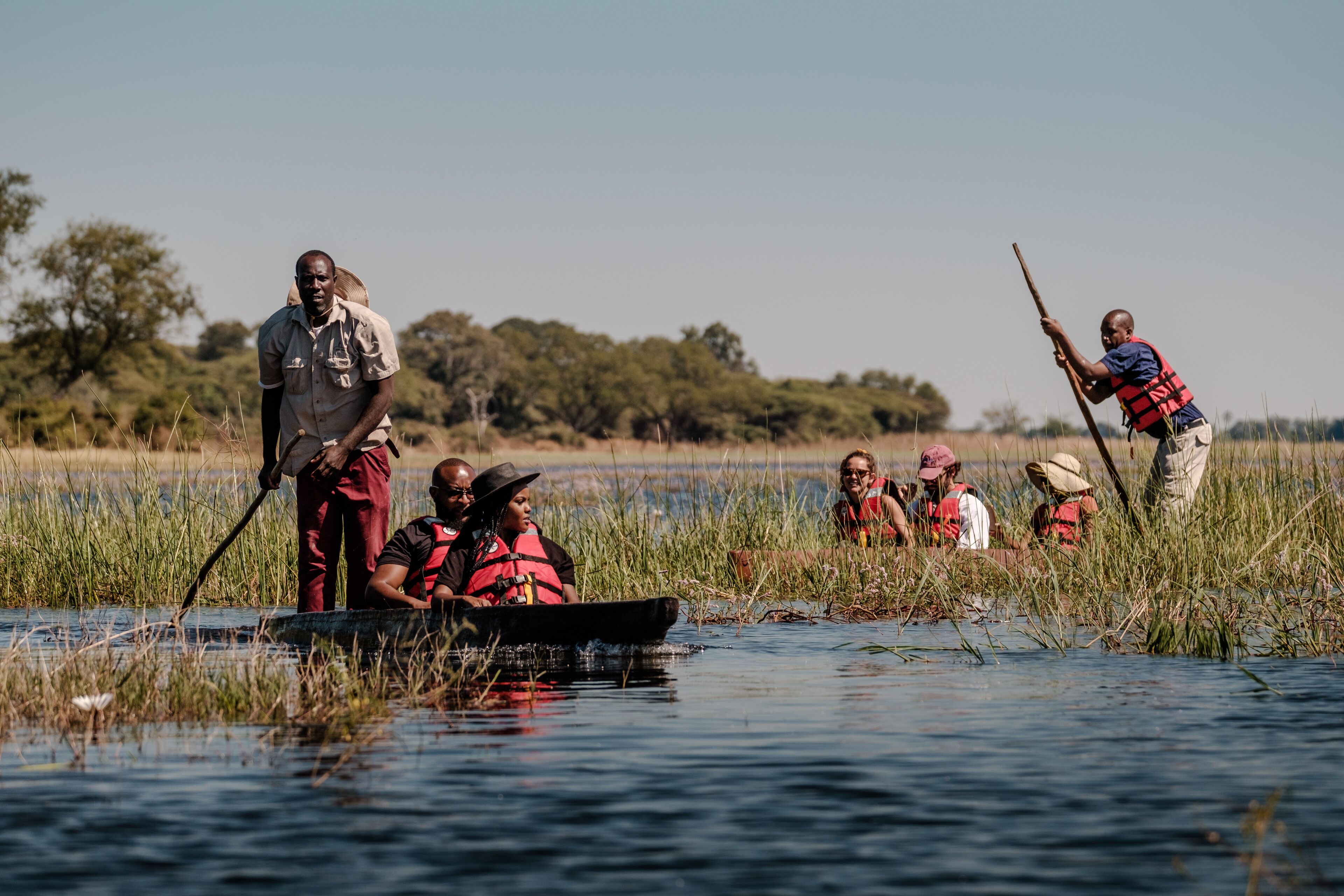 A group of people in a boat on a body of water surrounded by tall grass and trees.