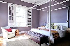 Quarto com uma cama de dossel, uma cadeira, um banco e uma janela com persianas.