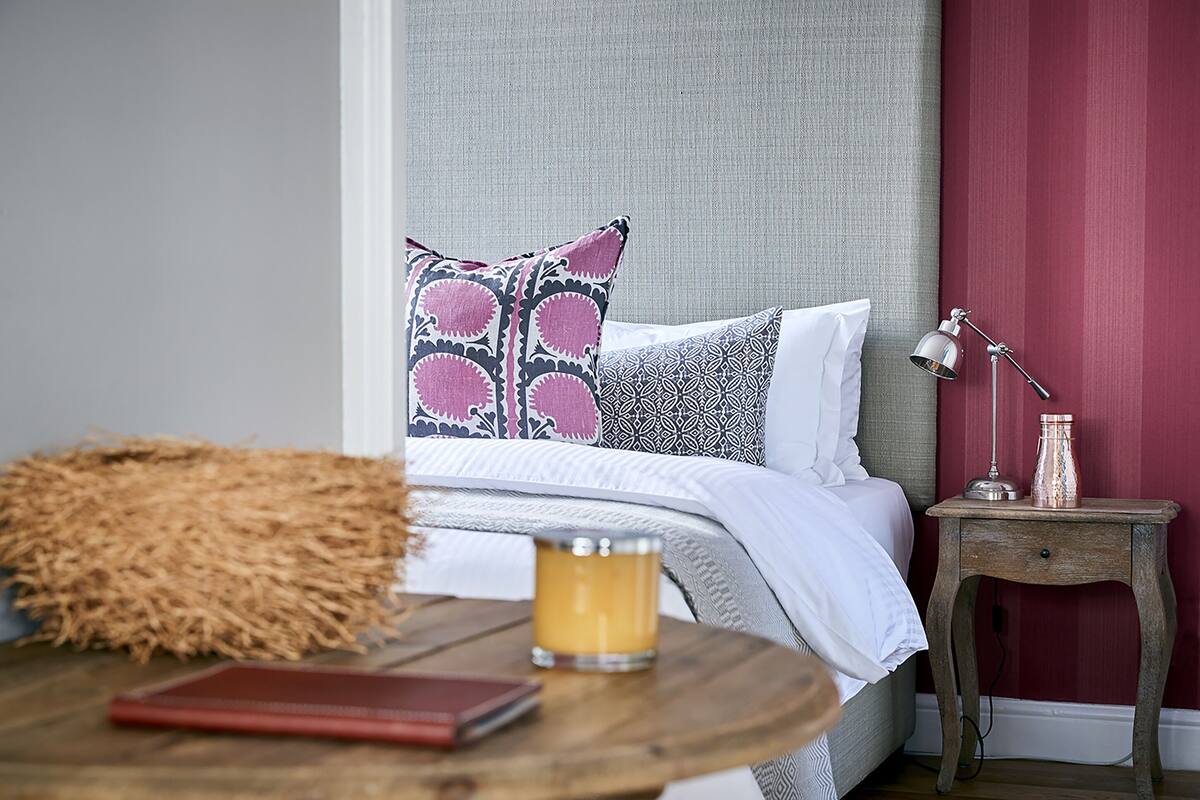 A neatly made bed with patterned pillows, a bedside table with a candle, a lamp, and a small decorative item.
