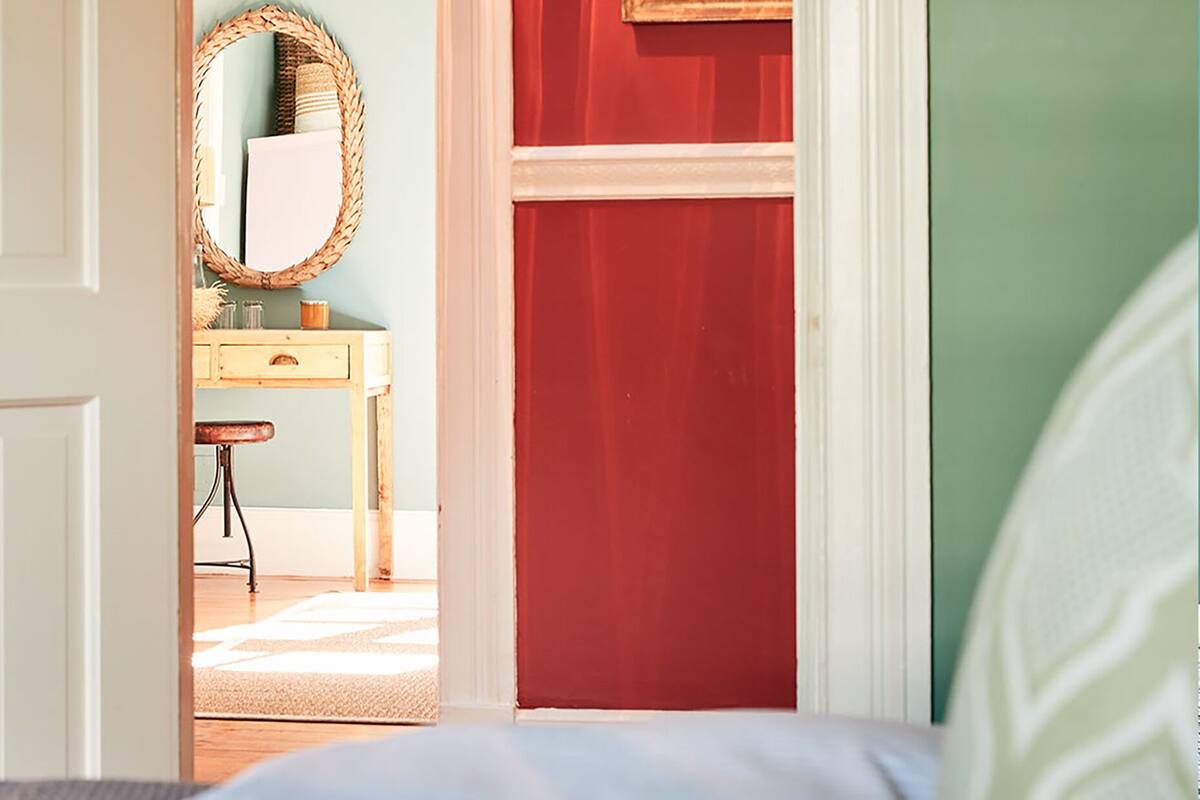 A room with a white door, a mirror, a wooden dresser, and a red wall.
