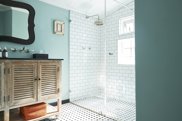 A bathroom with a wooden vanity, a glass shower enclosure, and a tiled floor.