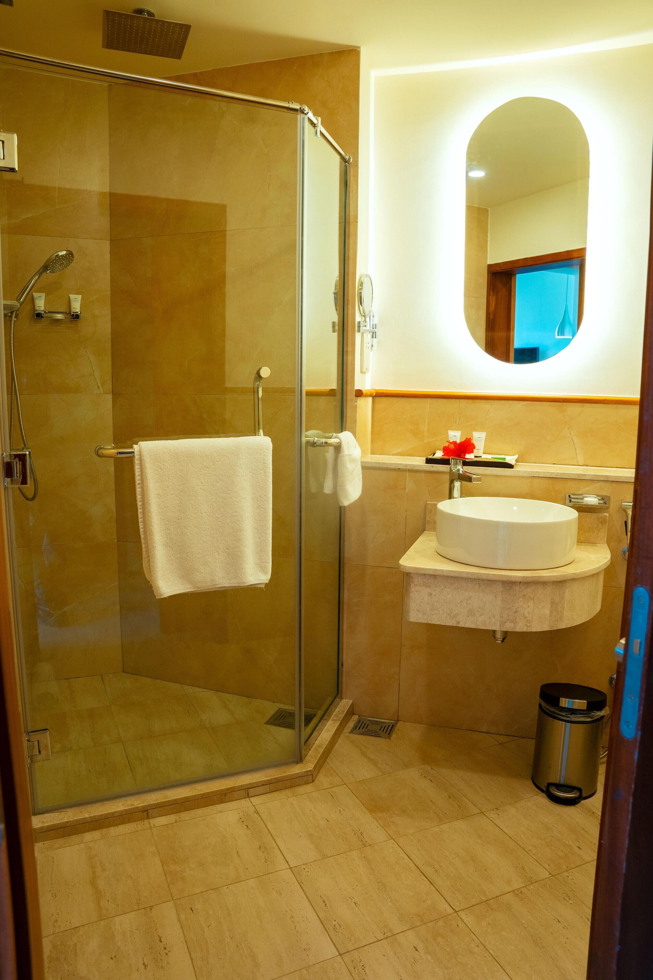 Un bagno con doccia vetrata, lavandino con specchio e cestino.