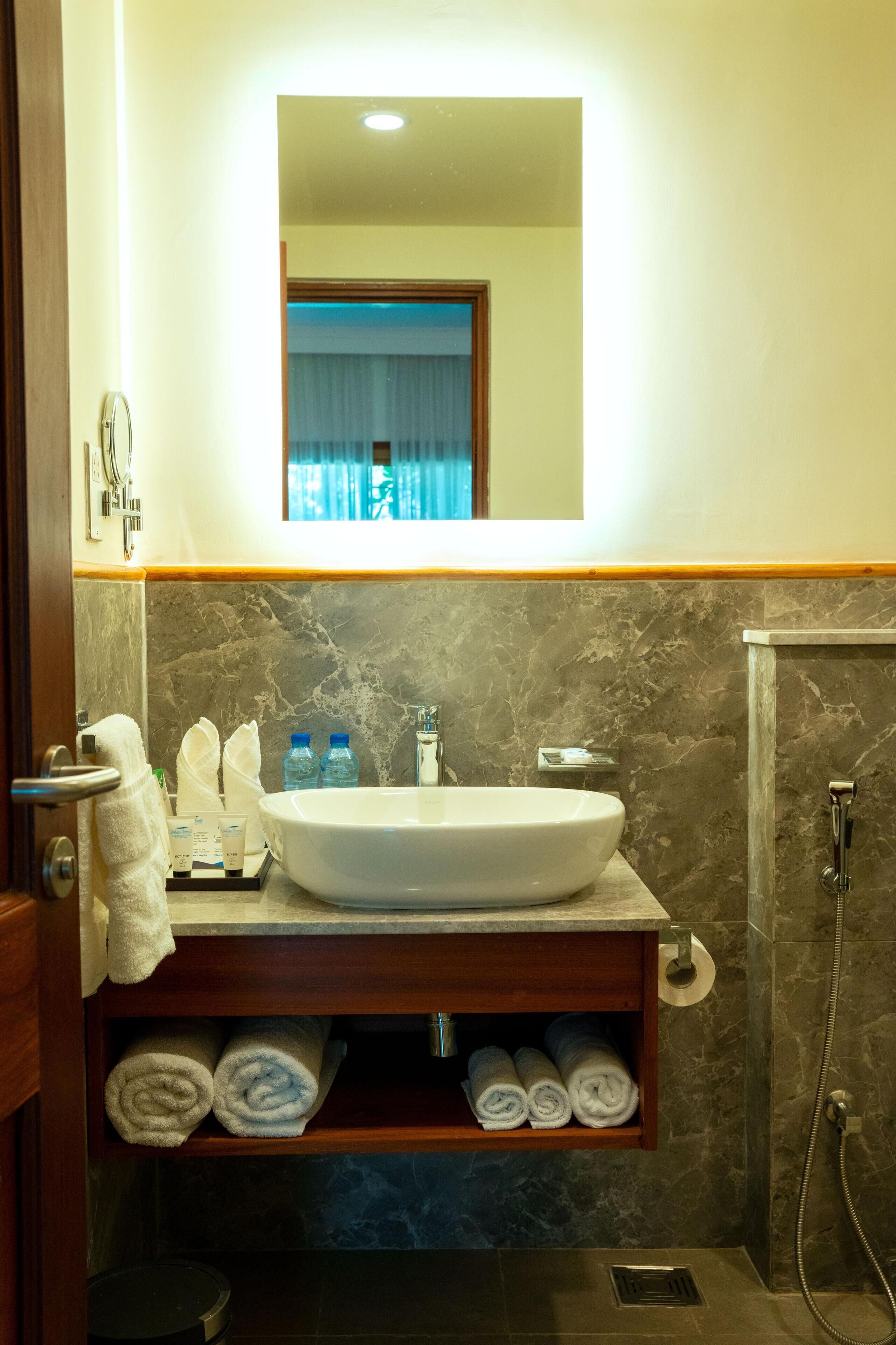 A bathroom with a marble wall, a sink, a mirror, and a towel rack with towels.