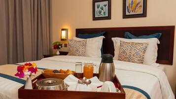 A neatly made bed with a tray of breakfast items, including a coffee pot, a pitcher of juice, and a bowl of fruit.