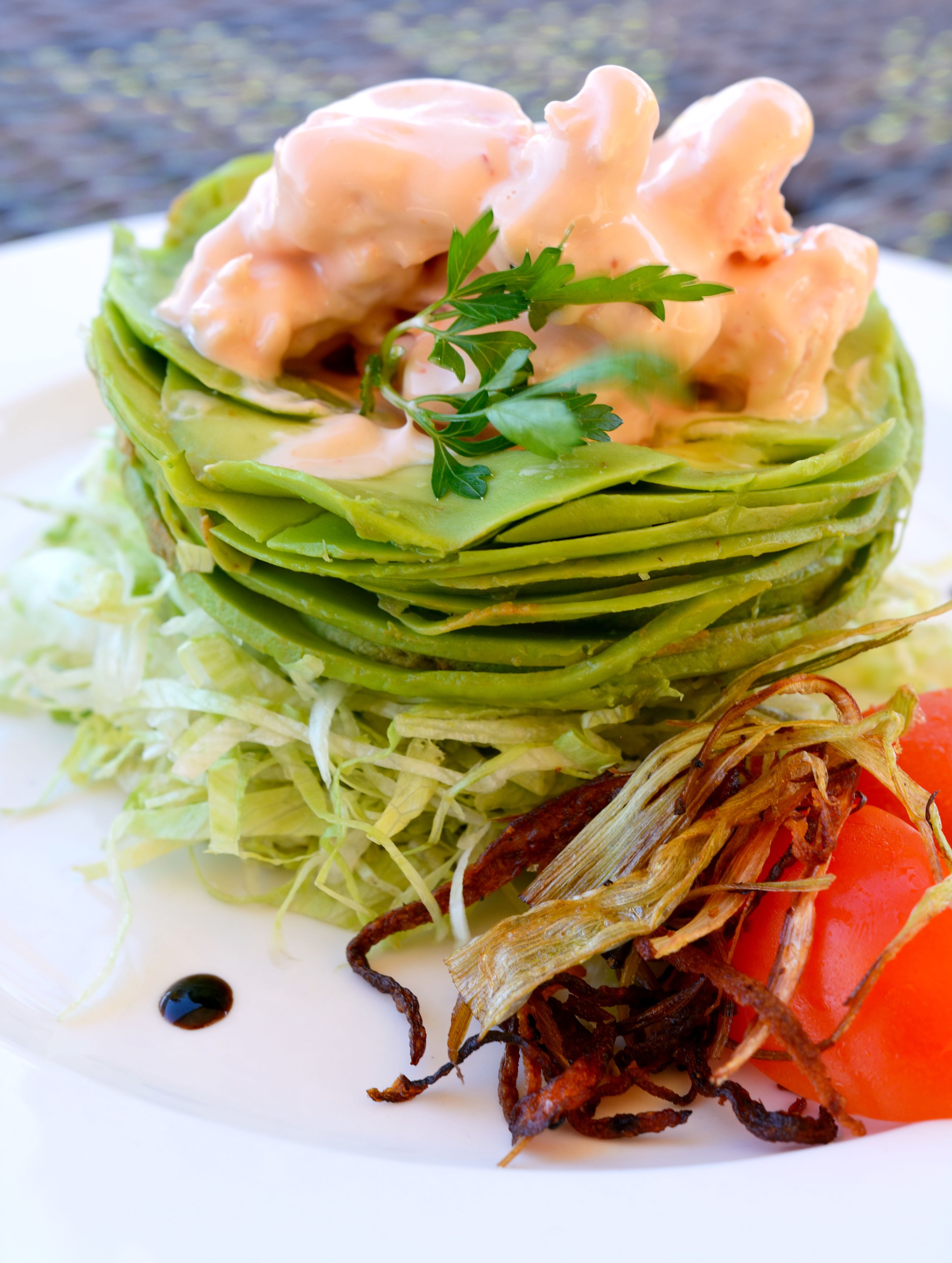 A layered salad with greens, a tomato, and a dollop of sauce, garnished with parsley.