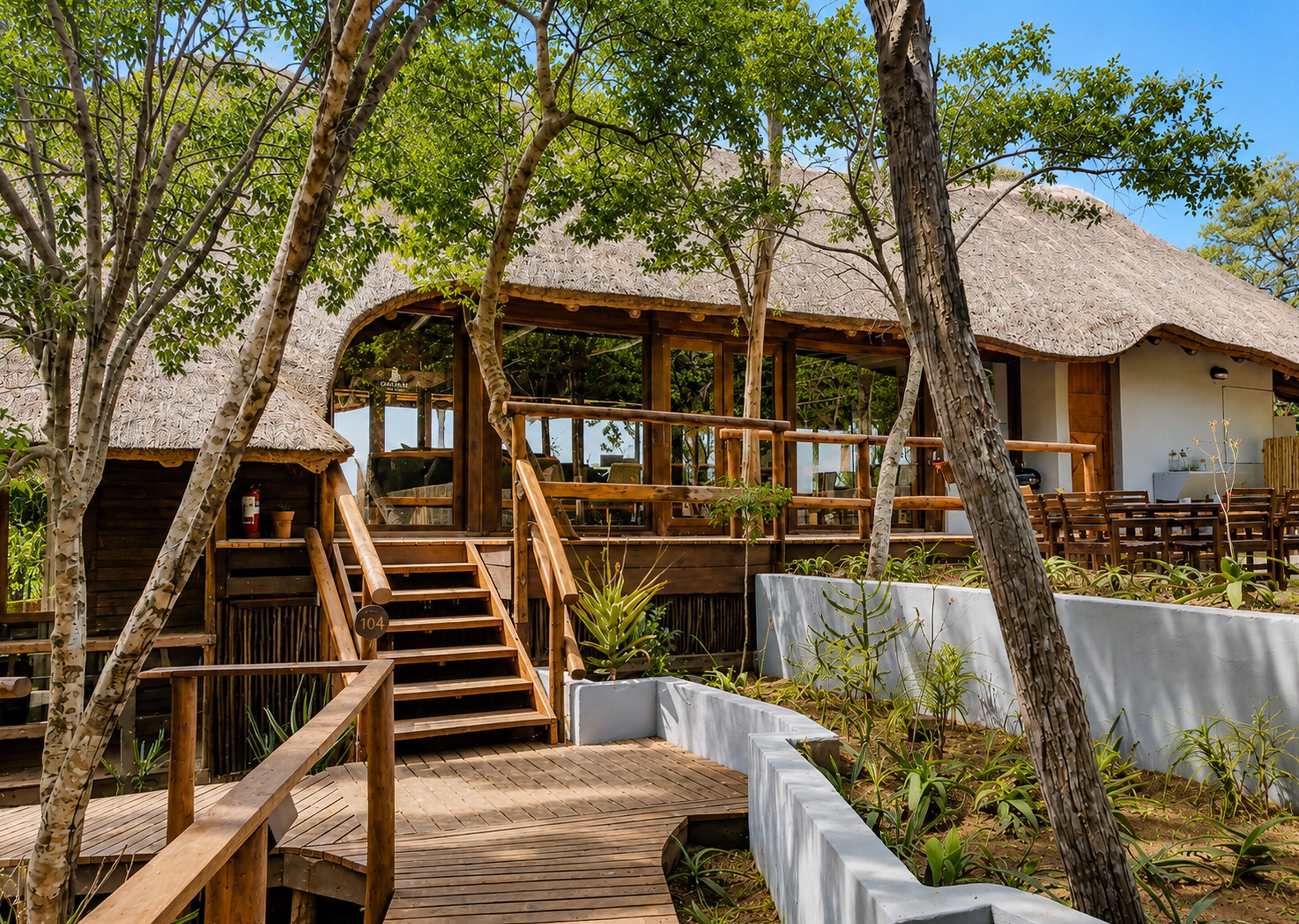 A wooden deck leading to a thatched-roof building with multiple windows and a staircase.