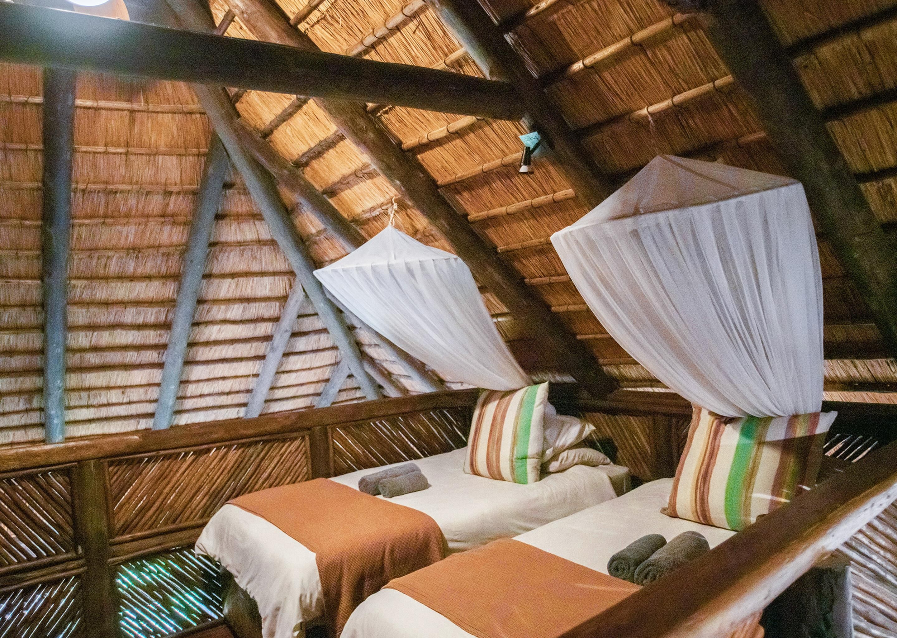 Una habitación con dos camas, cada una con dosel, y techo de paja.