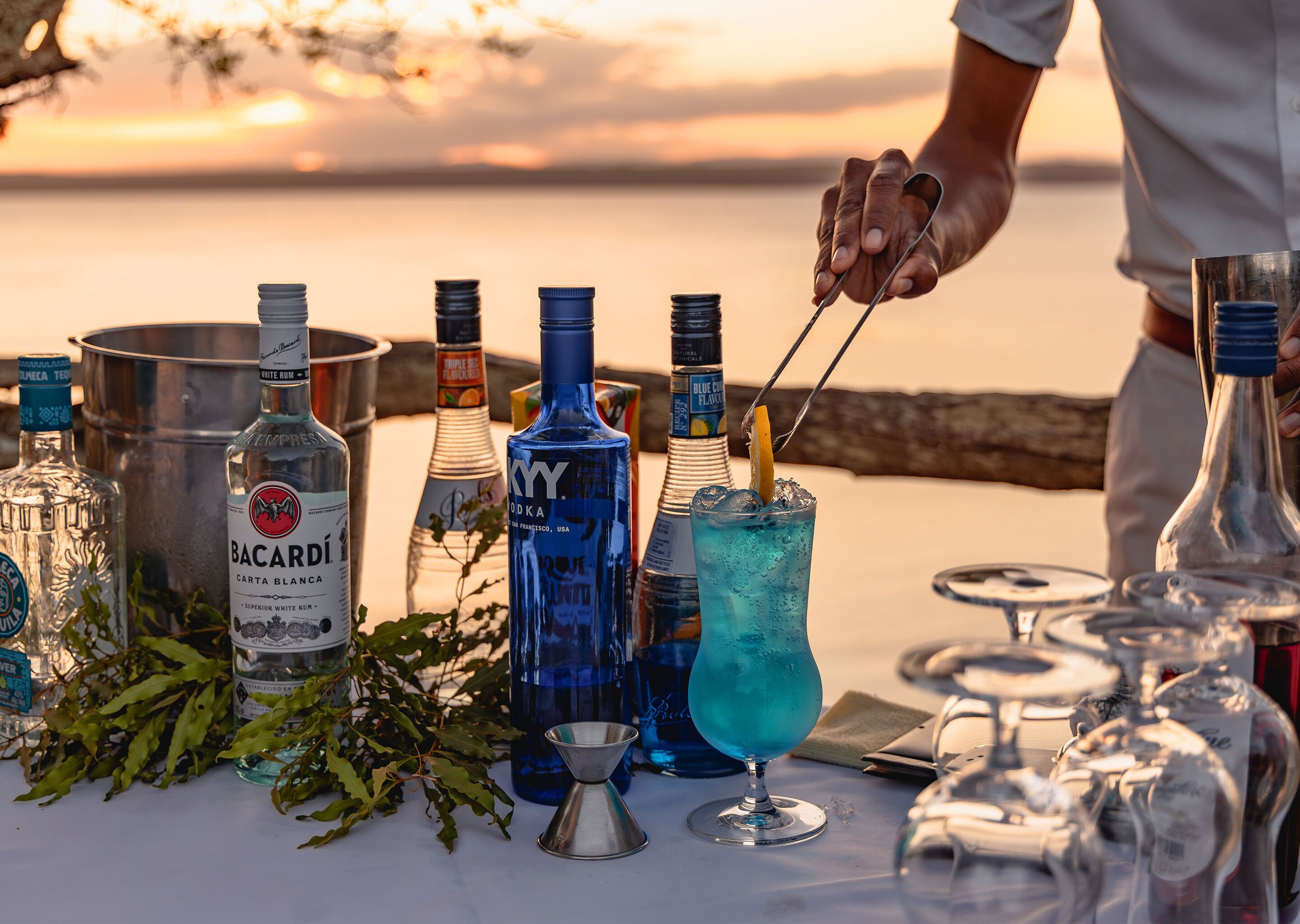 Una mesa con varias botellas de alcohol y una persona sirviendo una bebida.