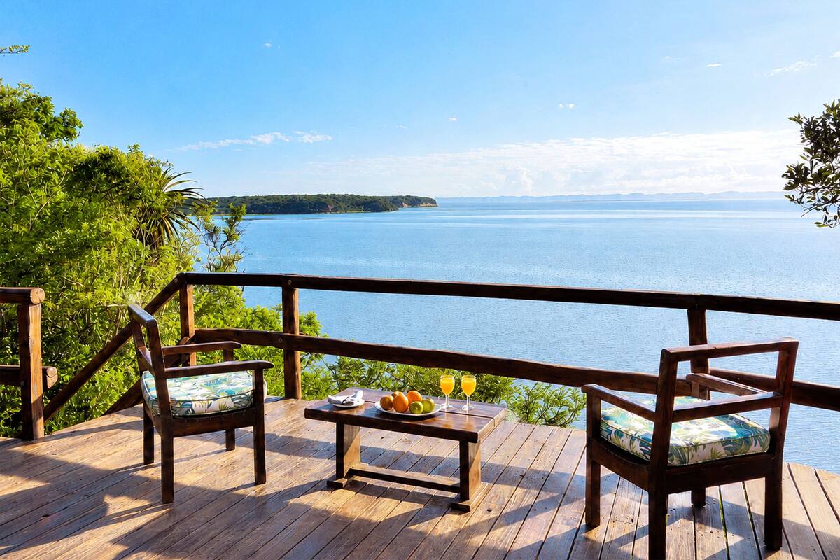 Une terrasse en bois avec deux chaises et une table, donnant sur une étendue d’eau et offrant une vue sur une terre lointaine.