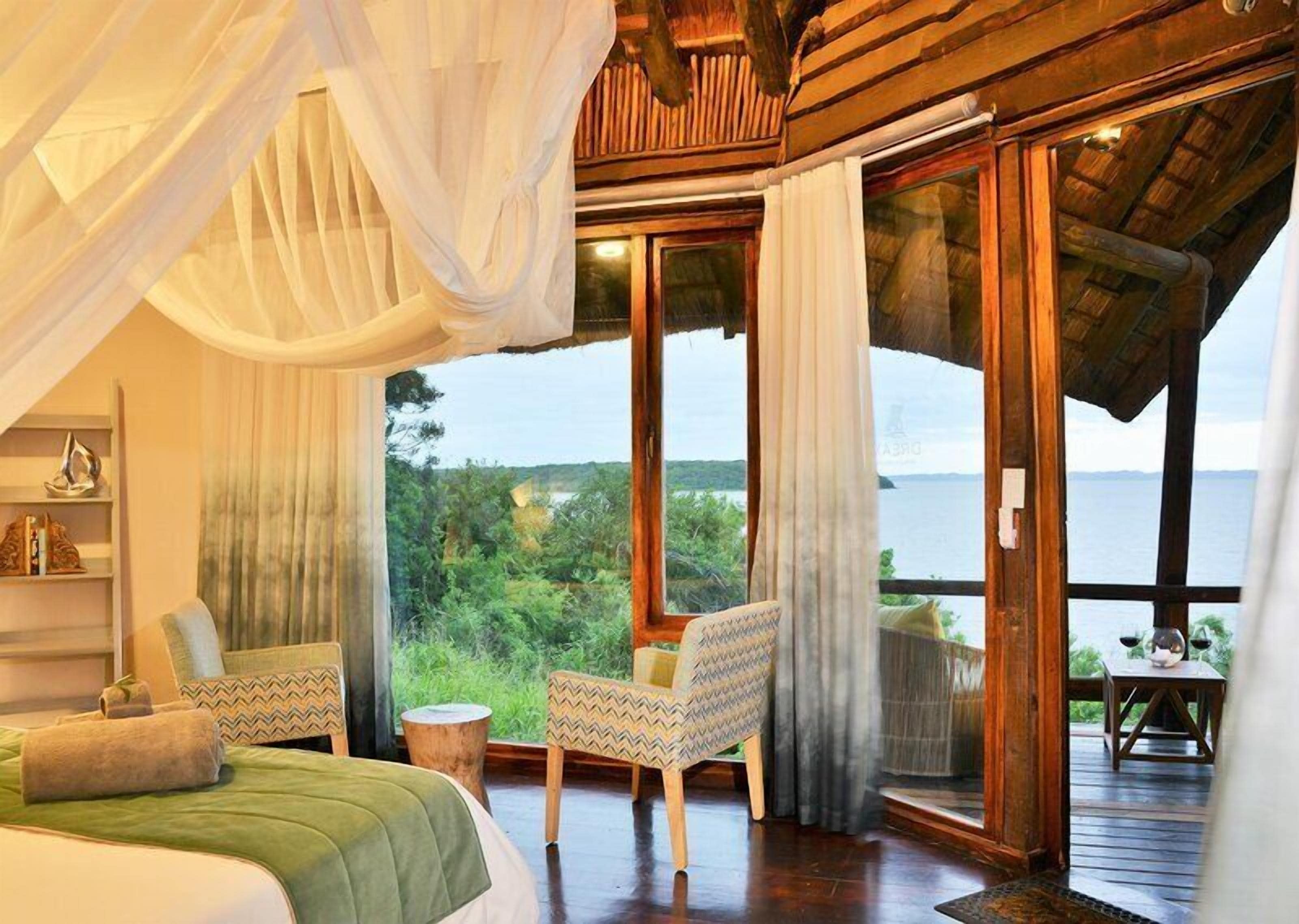 Une chambre avec un grand lit, une chaise, une petite table et une vue sur l’extérieur.
