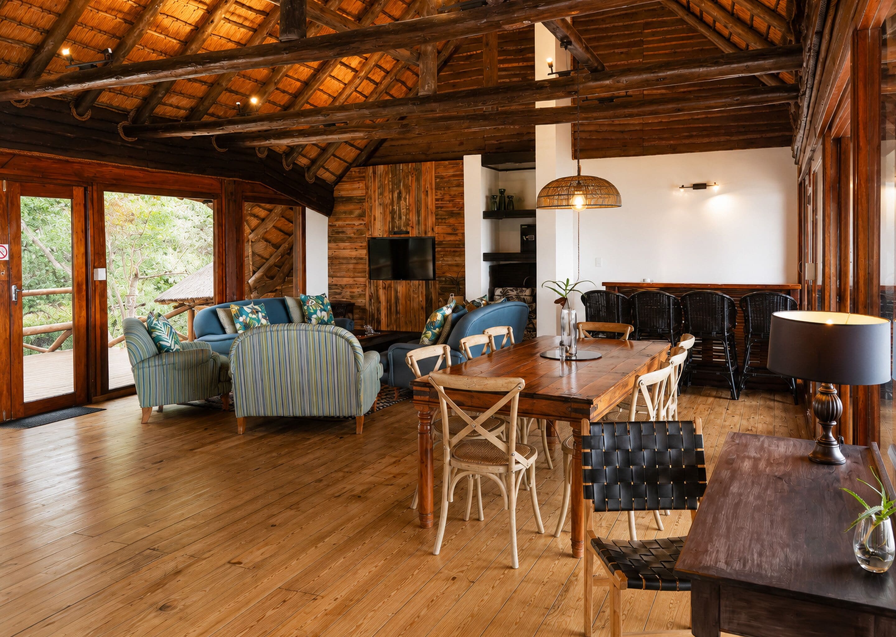 A rustic wooden interior with a dining area, sofas, and a TV.