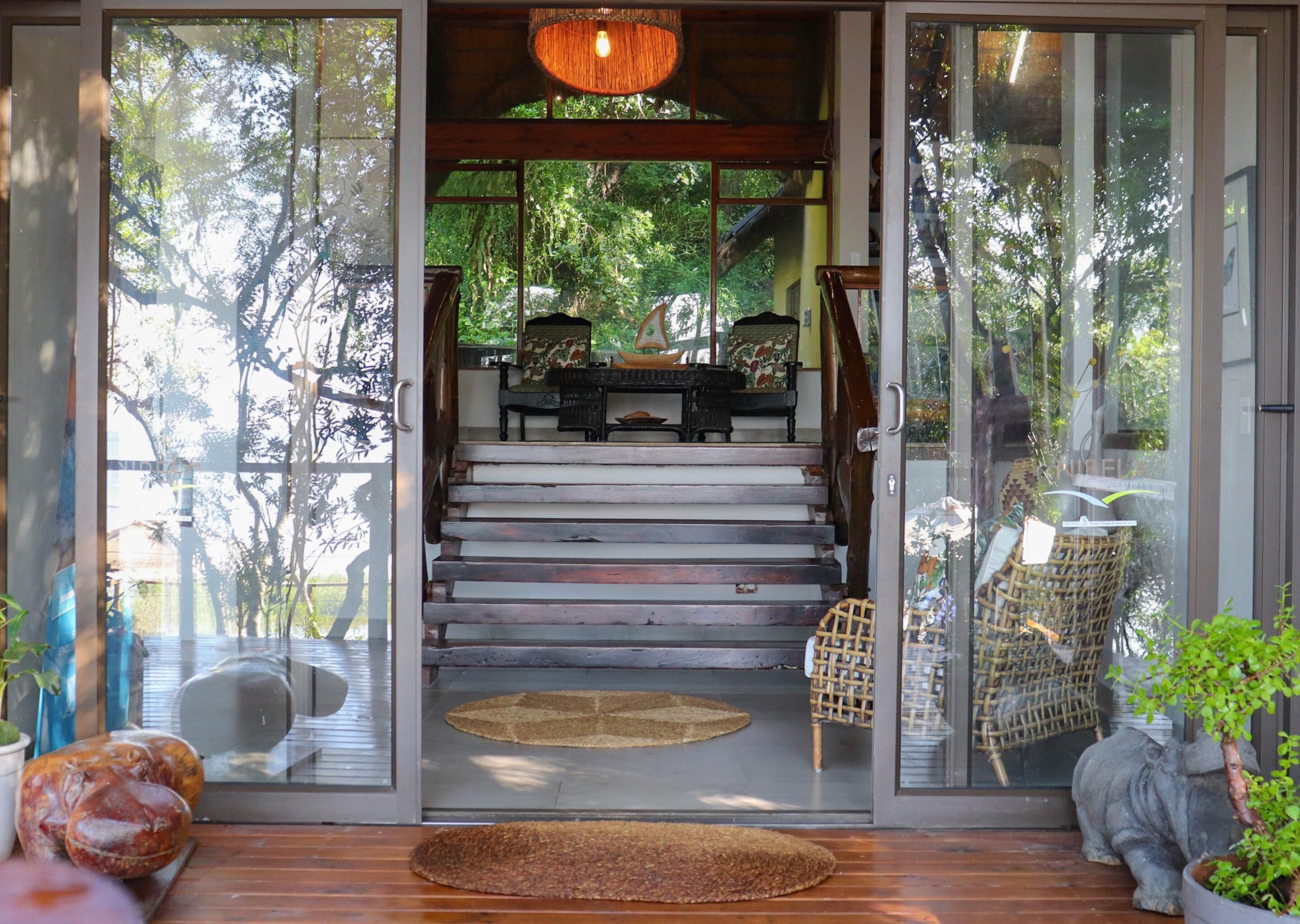 A wooden staircase leading to a room with a view of trees, a wicker chair, and a small elephant statue.