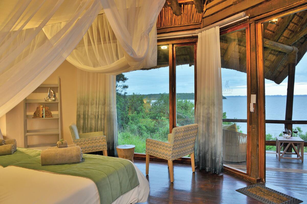 Une chambre avec un grand lit, un coin salon avec des fauteuils et une vue sur la mer.