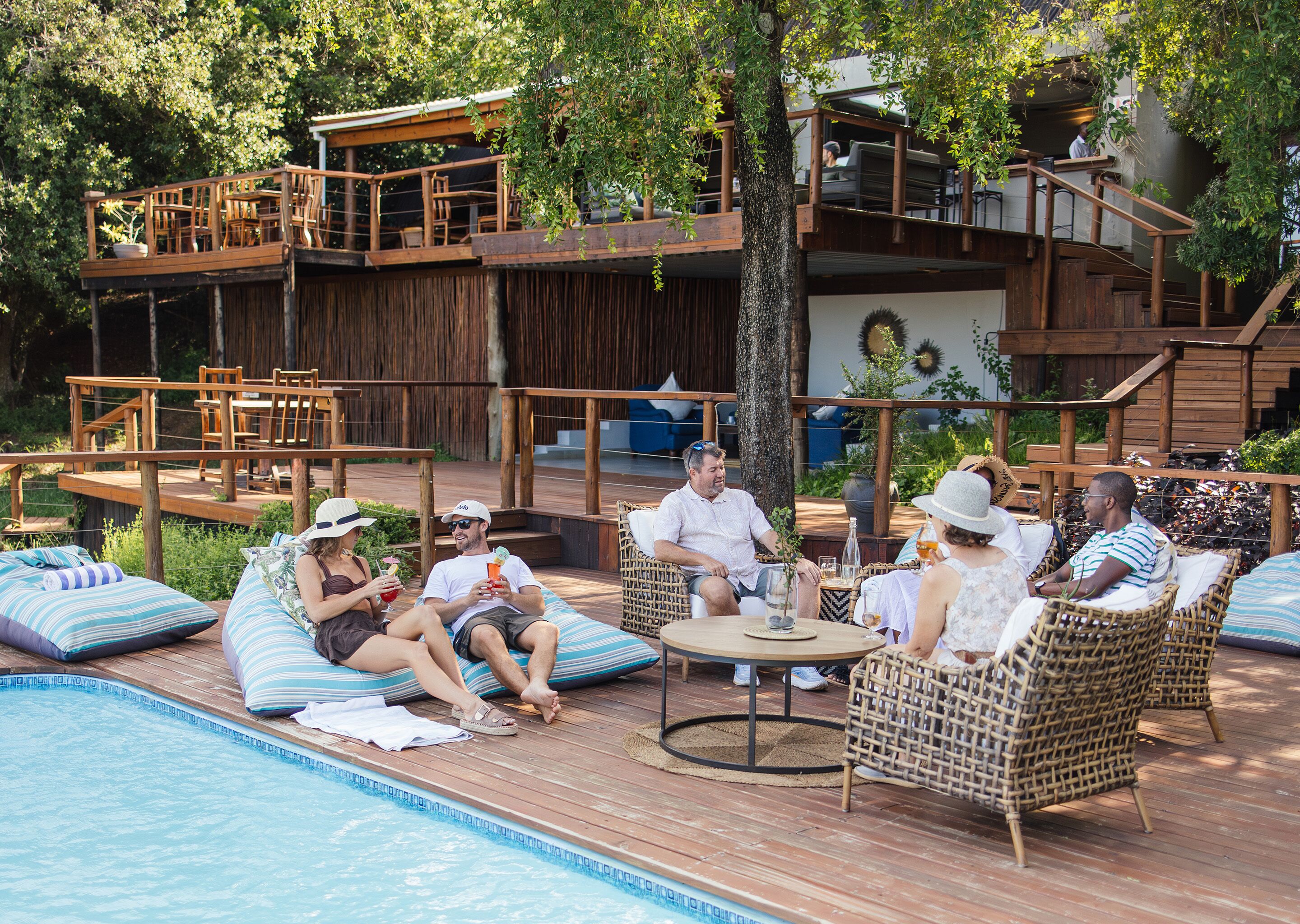A poolside area with wooden deck, lounge chairs, and a dining area with tables and chairs.