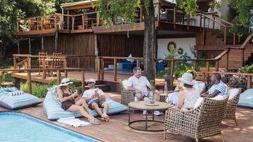 A poolside area with wooden deck, lounge chairs, and a dining area with tables and chairs.