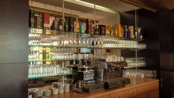 A bar area with shelves of glassware and bottles, a coffee machine, and stacked plates.