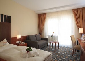 Habitación de hotel con cama, sofá, escritorio, silla y una pequeña mesa con un florero.